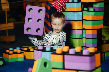 Küçük çocuk eğlence merkezinde büyük, yumuşak inşaat parçalarıyla oynuyor.