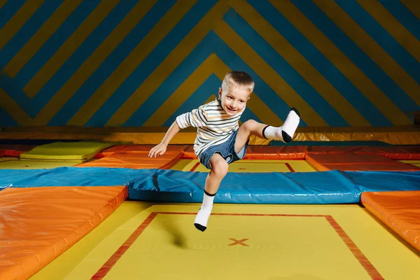 Lelkes fiú ugrál egy négyszögletes trambulinon a szórakoztató központban. — Stock Fotó