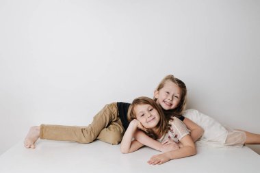 Neşeli kardeşler zıt yönlerde bir masada yan yana yatarlar. Oğlan kızı kucaklıyor