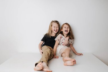 Gülen kardeşler masada birlikte oturuyorlar. Oğlan kıza sarılır, o da biraz eğilir.