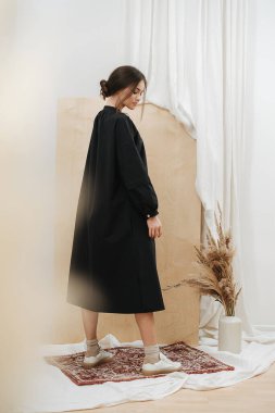 Siyah elbiseli mütevazı genç bir kadın küçük bir halıda duruyor.