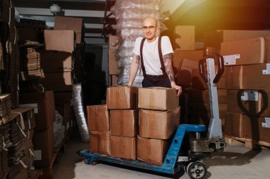 Mutlu bir erkek depo çalışanı bir kutu kutuya yaslanıyor.