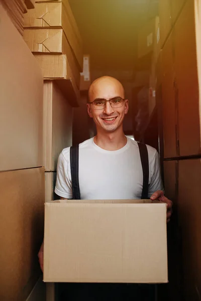 Friendly warehouse worker carrying box, standing between stacked boxes — 图库照片