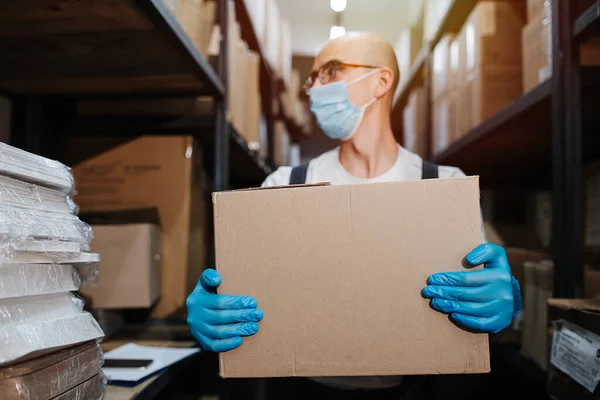 Tired warehouse worker carrying box, wearing mask and gloves. Selective focus