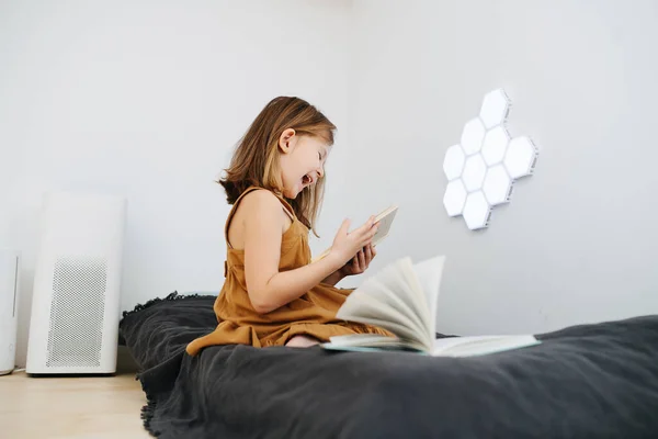 Een meisje dat op een bed zit leest een boek en lacht — Stockfoto