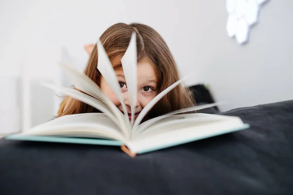 Close-up portrait of 6-year-old girl, shot through open book — Stock Photo, Image