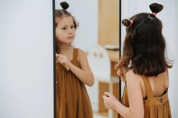 Girl looks after her hair, combs in front of a mirror — Stock Photo, Image