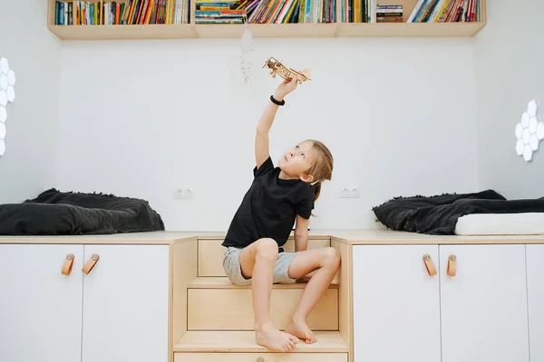 Νεαρό αγόρι παίζει με ένα ξύλινο αεροπλάνο στο παιδικό δωμάτιο — Φωτογραφία Αρχείου