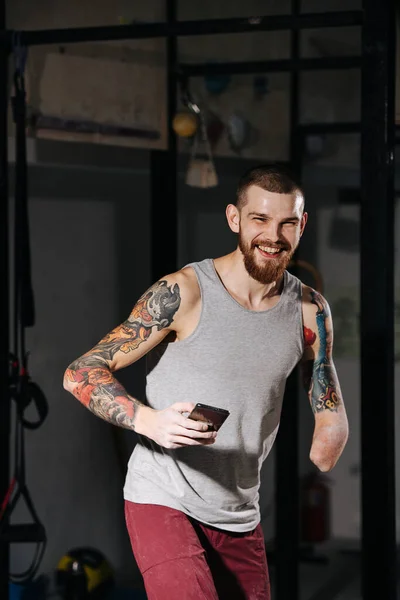 Gelukkige jonge gehandicapte armloze man in een trainingsruimte met een telefoon in de hand — Stockfoto