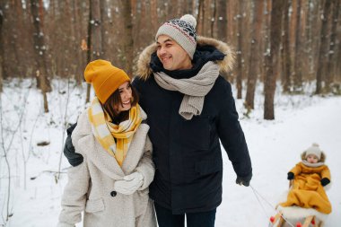 Kışın ormanda yürüyüşe çıkmış bir çift kızakla bir çocuğa biniyor.