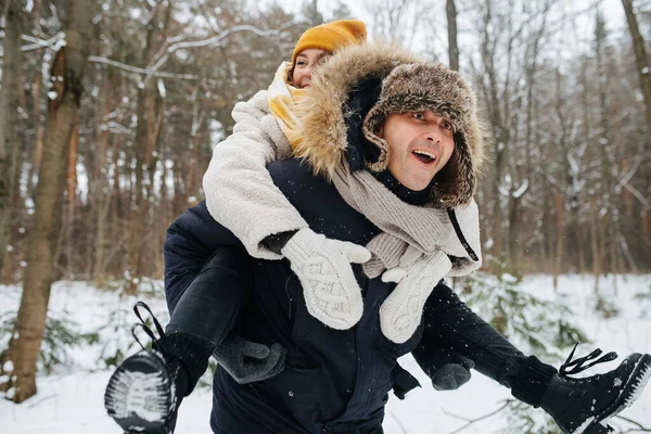 Молода щаслива пара. Жінка їде на людині назад у засніженому зимовому лісі . — стокове фото