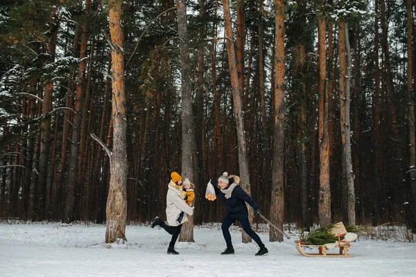 Молода жінка з дитиною в руках біжить назустріч чоловікові в зимовому лісі — стокове фото