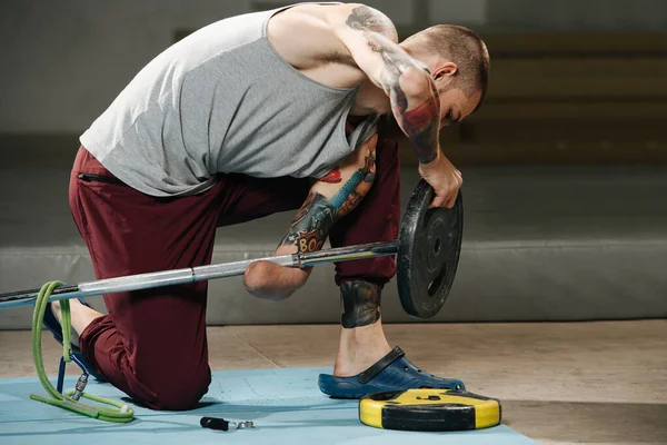 Keen hurched gehandicapte armloze man met tatoeages zetten schijf op een lange halter — Stockfoto