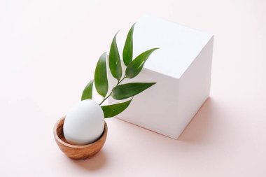 Beyaz bir kağıt küpün yanında pembe bir yüzey üzerinde ahşap yumurta standı.