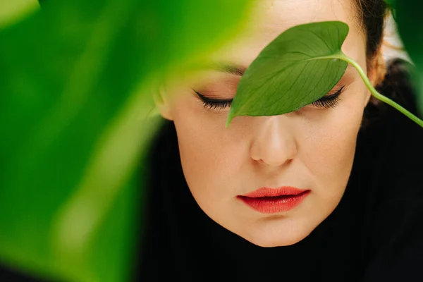 Sinnliches Mädchen mit schönem Make-up und roten Lippen zwischen grünen Blättern — Stockfoto