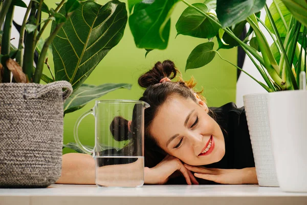 A smiling girl lay down on the table and closed her eyes among the green leafs — Stock Photo, Image