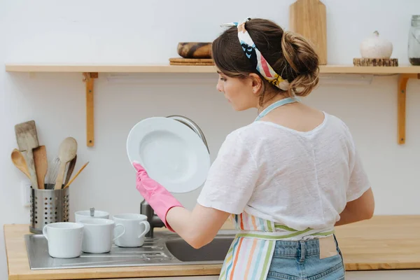 Bulaşıkları eldivenle yıkayan genç kız, temiz bir tabak koyar. — Stok fotoğraf