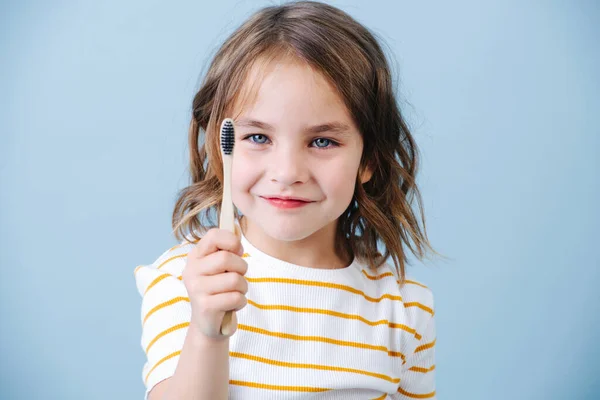 Menina sorridente com escova de dentes de bambu na mão, retrato em um fundo azul — Fotografia de Stock