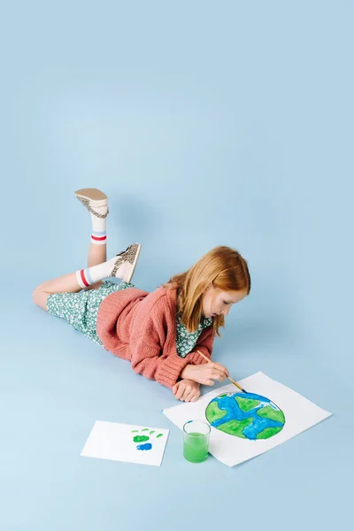Chica pelirroja tirada en el suelo dibuja un planeta verde-azul —  Fotos de Stock