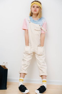 Genç kız duvara yaslanmış ve elleri ceplerinde duruyor.