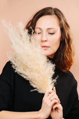 Siyah elbiseli bir kız, elinde kuru bitkiler var.