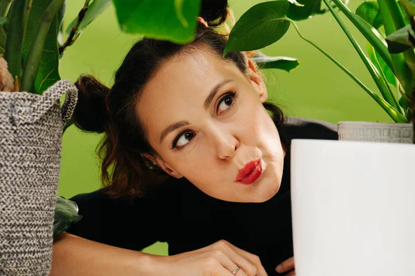 Assobios menina, retrato entre folhagem verde de plantas domésticas — Fotografia de Stock