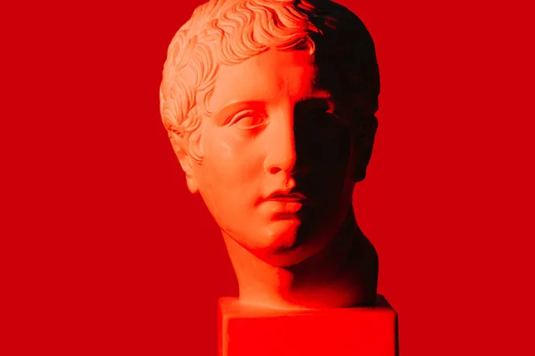 Rood-verlichte half-schaduwrijke marmeren hoofd van de jongeman over rode achtergrond. — Stockfoto