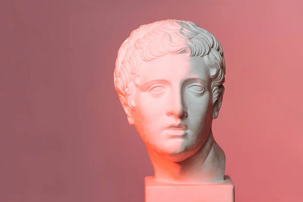 Frontal view of a white marble head of young man over red-lit pink background. — Stock Photo, Image