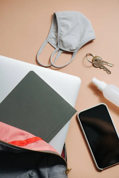 Backpack with laptop and notebook in it. Other everyday items on a peach surface