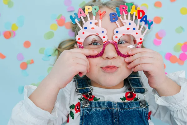 Happy little girl lies on a floor, holding onto her birthday glasses — Stock Photo, Image