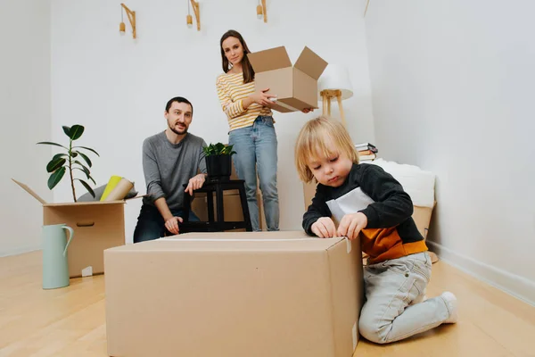 O conceito de mudança para uma nova casa, a família está envolvida em caixas de desempacotamento — Fotografia de Stock