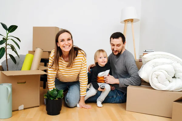 Familia joven sentada en una vivienda nueva entre cajas — Foto de Stock