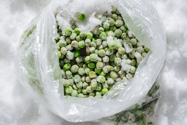Green frozen peas covered with tiny ice crystals in a plastic bag. top view.