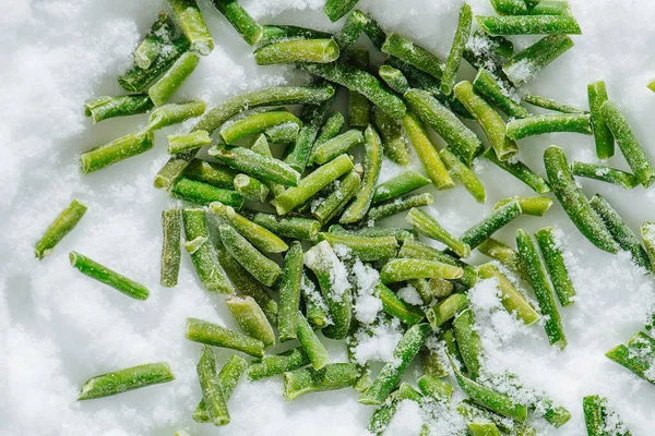 Déversement de haricots verts congelés sur une glace broyée. vue de dessus. — Photo