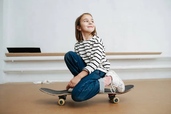 Jolie petite fille assise sur un genou sur une planche à roulettes, posant pour une photo — Photo