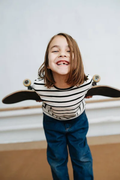 Bezzubá holčička pózuje s skateboardem, hraje roztomile, naklání se dopředu — Stock fotografie