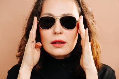 Müsrif orta yaşlı kadın güneş gözlüğünü takıyor, kameraya bakıyor.