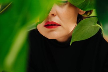 Büyük bitki yapraklarının arkasında yorgun, orta yaşlı bir kadının kırmızı dudakları..