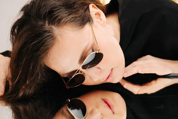 Schöne Frau mittleren Alters mit Sonnenbrille auf einem stark reflektierenden Tisch liegend — Stockfoto