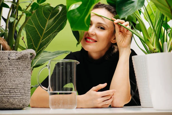 Mulher sorrindo brincalhão sentada atrás de uma mesa entre grandes vasos com plantas — Fotografia de Stock