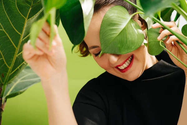 Awkward middle aged woman with closed eyes big plant leaves getting in her face — Stock Photo, Image