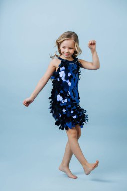 Parlak mavi skalalı elbisesi olan, yalın ayaklı komik kız dans ediyor.