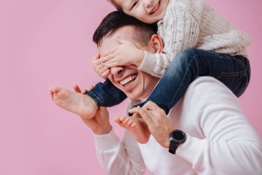 Sevgi dolu oğul babasının omuzlarında oturuyor, gözlerini kapatıyor. Koyu pembe üzerine