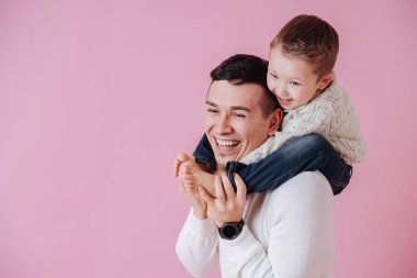 Yapışkan çocuk babasının omuzlarında, düşmemeye çalışıyor. Koyu pembe üzerine