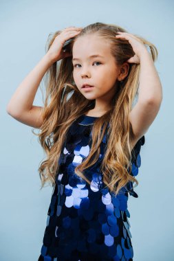 Parlak mavi pullu elbisesi olan sevimli kız dağınık saçlarıyla ilgileniyor.