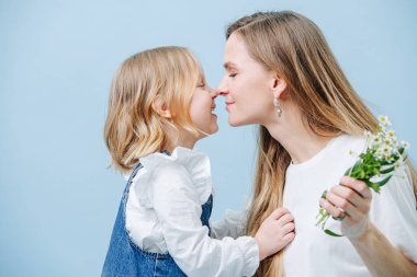 Küçük kız, annesi tarafından bir buket vahşi papatya verdiği için kucaklanıyor.