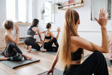 Eğitmenin yardımıyla yoga yapan bir grup kadın, yan çevirme yapıyor.