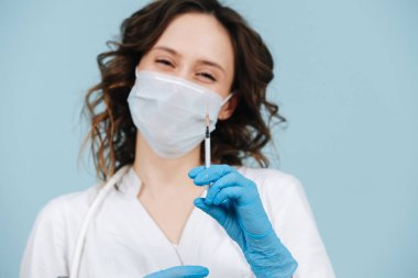 Gülen hemşire aşı enjeksiyonu için şırıngayla poz veriyor. Mavi arkaplan.