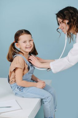 Gülümseyen doktor steteskopla küçük mutlu kızı muayene ediyor. Yan görünüm.