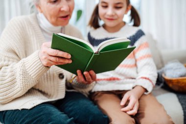 Sevgili büyükannem torunuyla kanepede oturuyor. Onlar birlikte bir kitap okuyorlar. Objeye odaklan, yüzler bulanık.